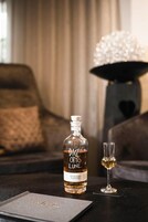 Una botella de vino Distilleria Marz Zadori DOCG de 1949, una copa de vino y una lámpara decorativa sobre una mesa.