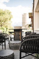 An outdoor seating area with wicker chairs and tables, a stone table, and a view of a building with a tower.