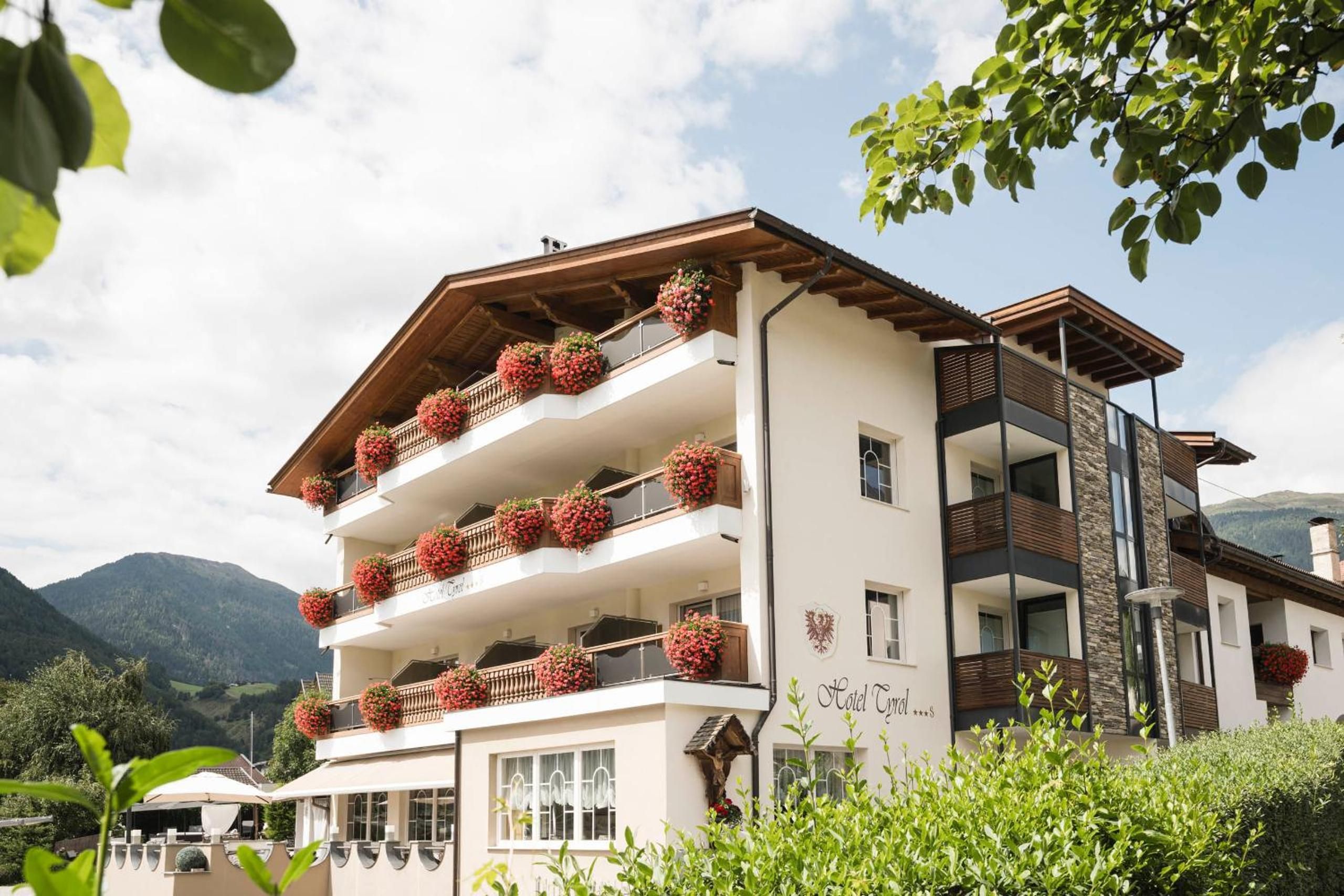 Ein mehrstöckiges Hotel mit Balkonen, die mit Blumenkästen geschmückt sind, vor einer Bergkulisse.
