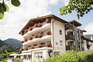 A multi-story hotel with balconies adorned with flower baskets, set against a mountainous backdrop.