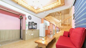 Un hall d’hôtel avec un escalier en bois, un canapé rouge, une table basse en bois et, au fond, un coin cuisine.