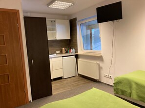 Quarto com cozinha compacta, janela com vista, televisão na parede e duas camas com toalhas verdes.