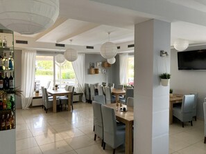 A modern dining area with multiple tables and chairs, a bar with bottles, and a TV mounted on the wall.