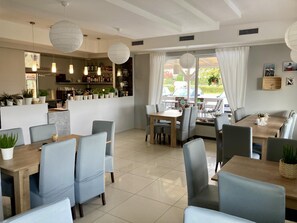 A modern dining area with multiple tables and chairs, a bar area with shelves of bottles, and large windows with curtains. - Hotel Solec (Gora Kalwaria)