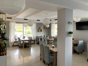 A modern dining area with multiple tables and chairs, a bar with bottles, and a TV mounted on the wall. - Hotel Solec (Gora Kalwaria)