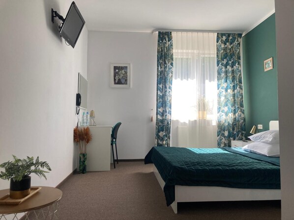 Quarto com cama, escrivaninha, cadeira, planta em vaso e janela com cortinas.
