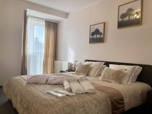 Una habitación de hotel con una cama grande, una mesita de noche con una lámpara y dos cuadros en la pared.