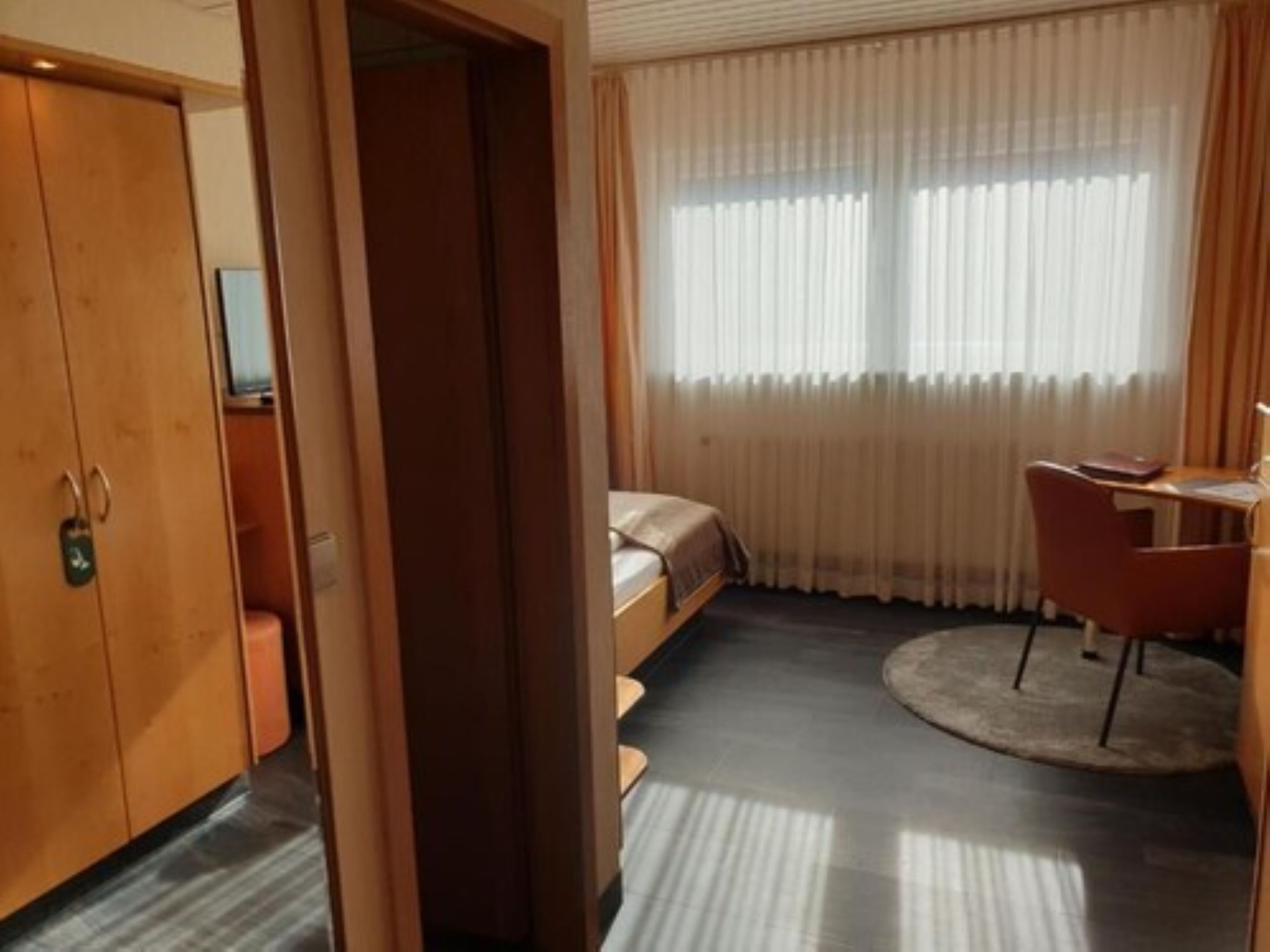 A hotel room with a bed, a desk, a chair, and a wardrobe.