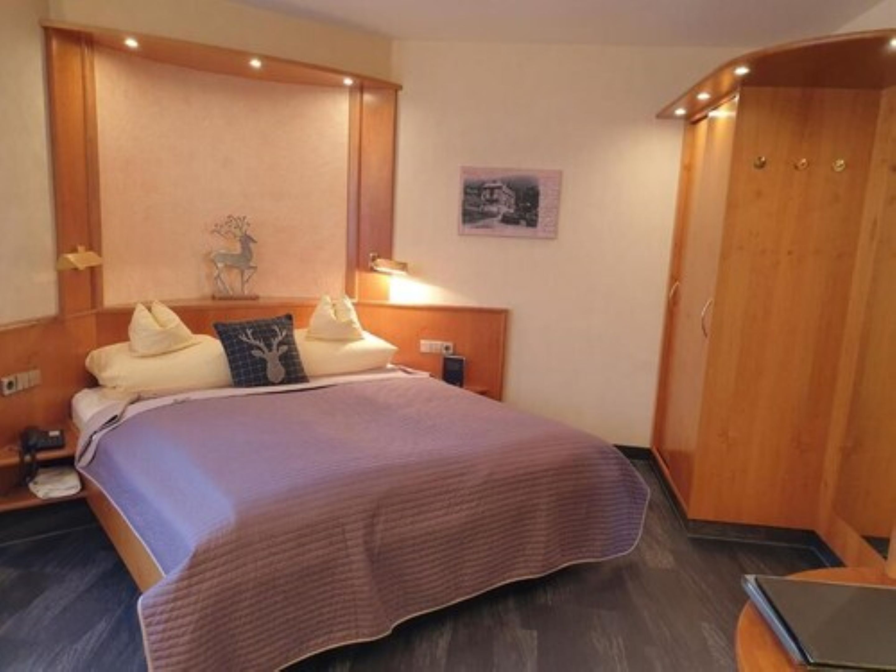 Un dormitorio ordenado con cama, lámparas de noche, una mesita de noche y un armario de madera.