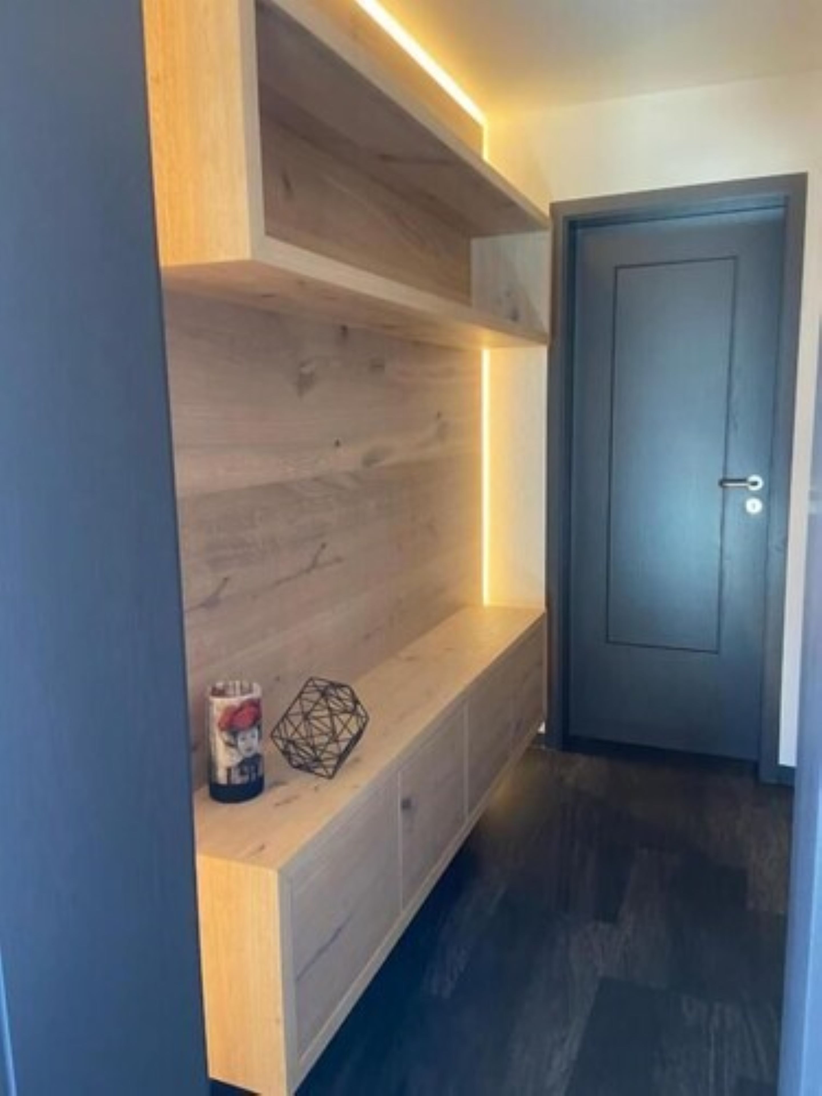 Un pasillo con un banco de madera, una puerta y un zócalo con luz.