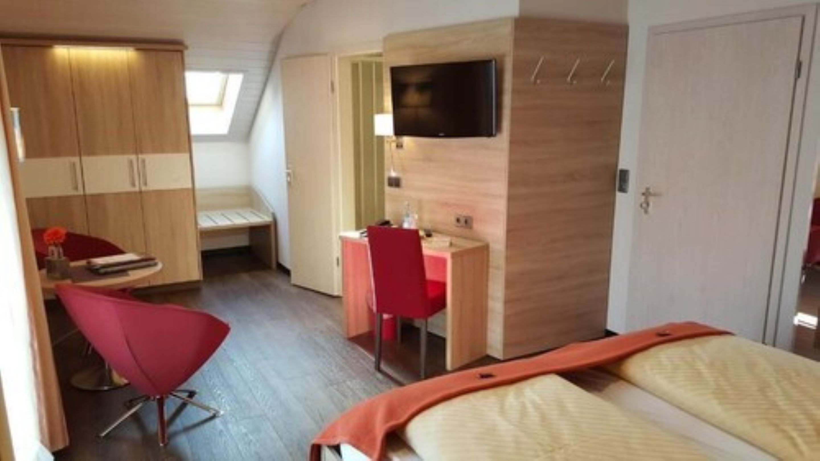 Ein kleines Zimmer mit Bett, Schreibtisch, Stuhl und Fernseher.