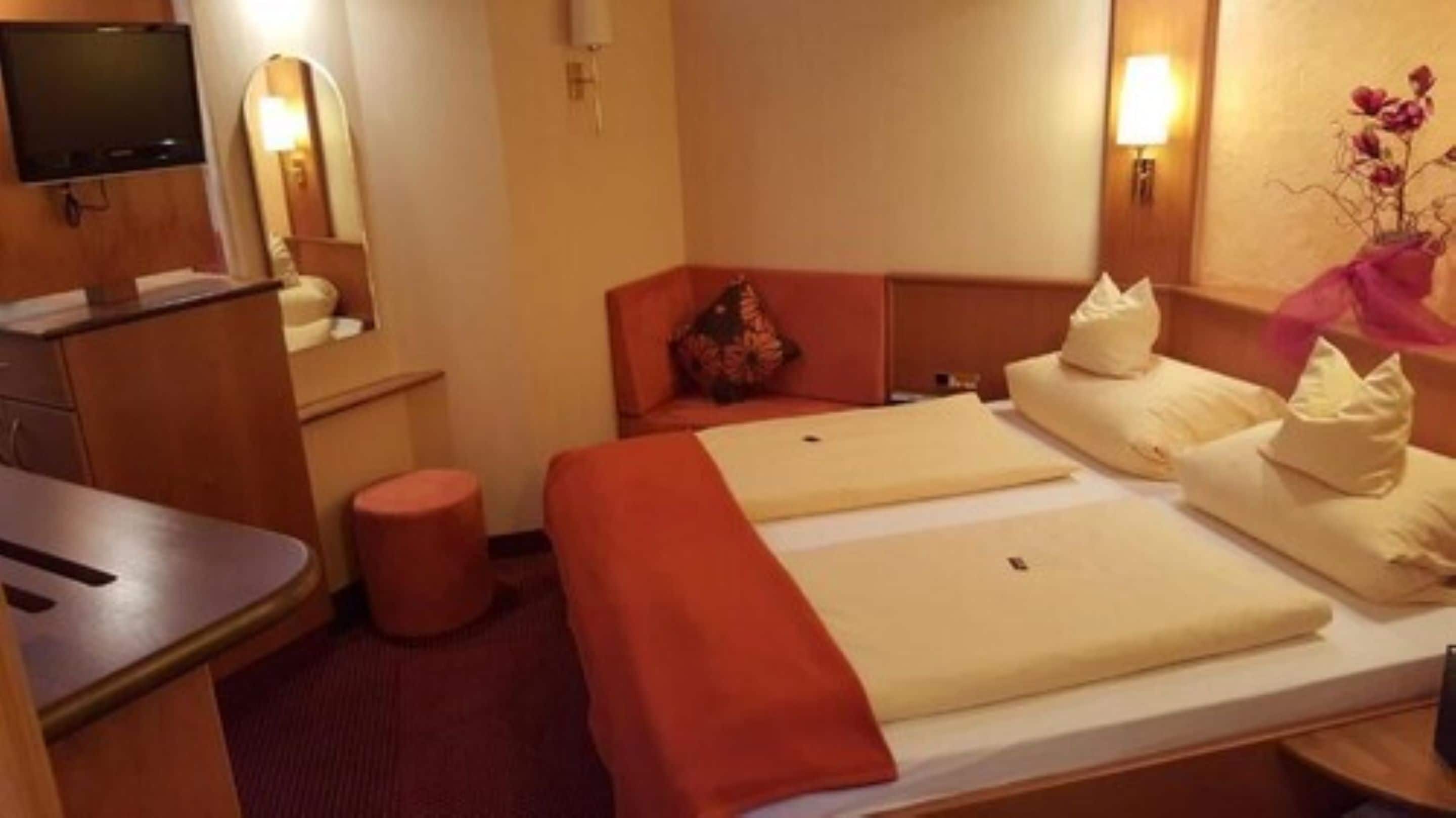 Habitación de hotel con dos camas, un escritorio, una silla, un taburete pequeño y un televisor.