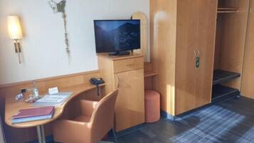 A compact hotel room with a wooden desk, a chair, a television, and a wardrobe.