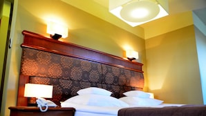 Habitación de hotel con cabecera estampada, dos lámparas de noche, un teléfono y una cama con ropa blanca.
