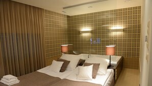 Una habitación de hotel con una cama grande, dos lámparas de noche y baldosas de pared cuadriculadas.