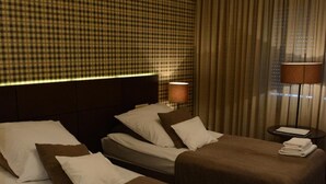 Habitación de hotel con dos camas, una pared a cuadros, una lámpara colgante grande y una ventana con cortinas.