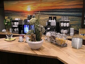 A reception area with a wooden counter, a large painting of a sunset, and various coffee and tea equipment.