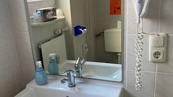 Ein Badezimmer mit einem weißen Waschbecken, einem Spiegel und einem an der Wand befestigten Föhn.