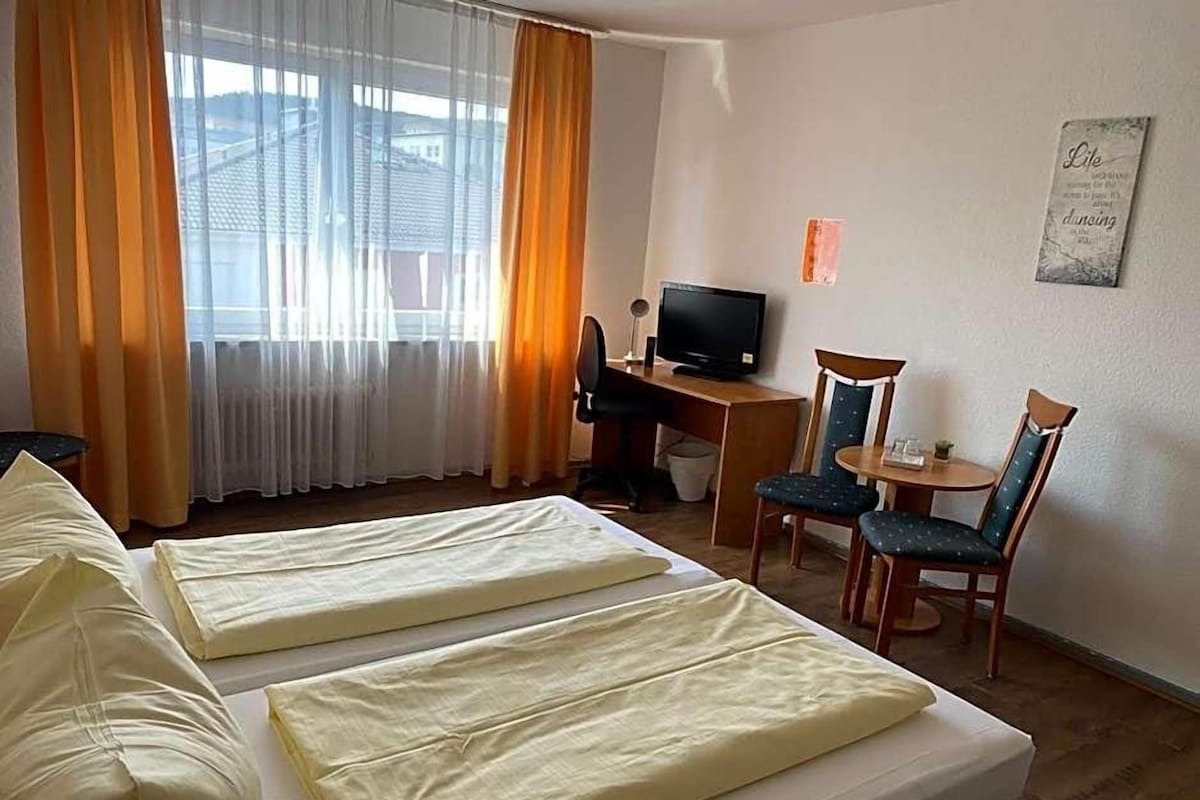 A hotel room with two beds, a desk with a computer, a chair, and a television.