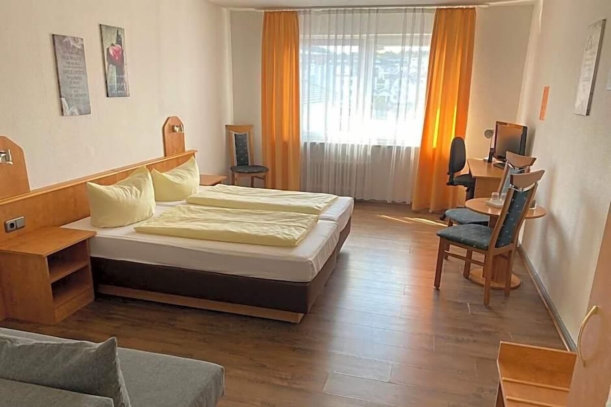 A hotel room with a bed, a desk, a chair, and a sofa.