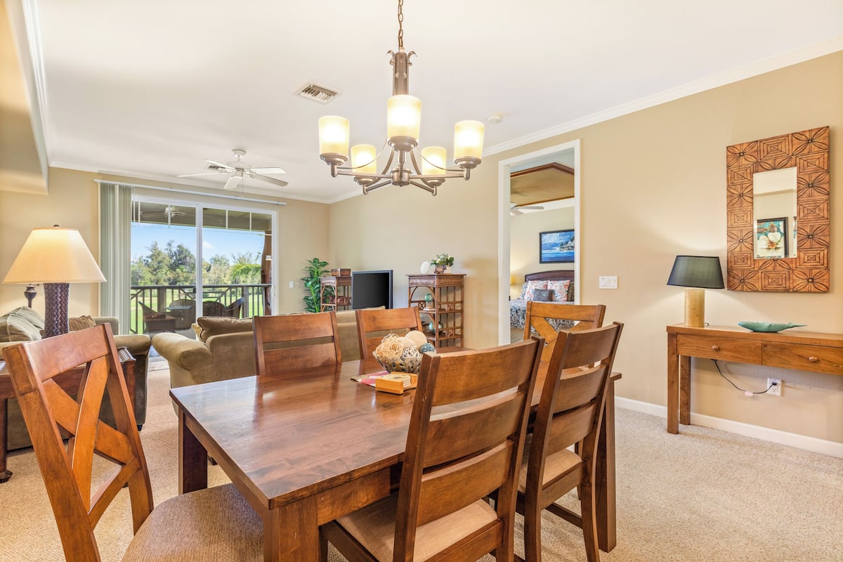 A dining area with a wooden table and chairs, a chandelier, and a view of the outdoors.