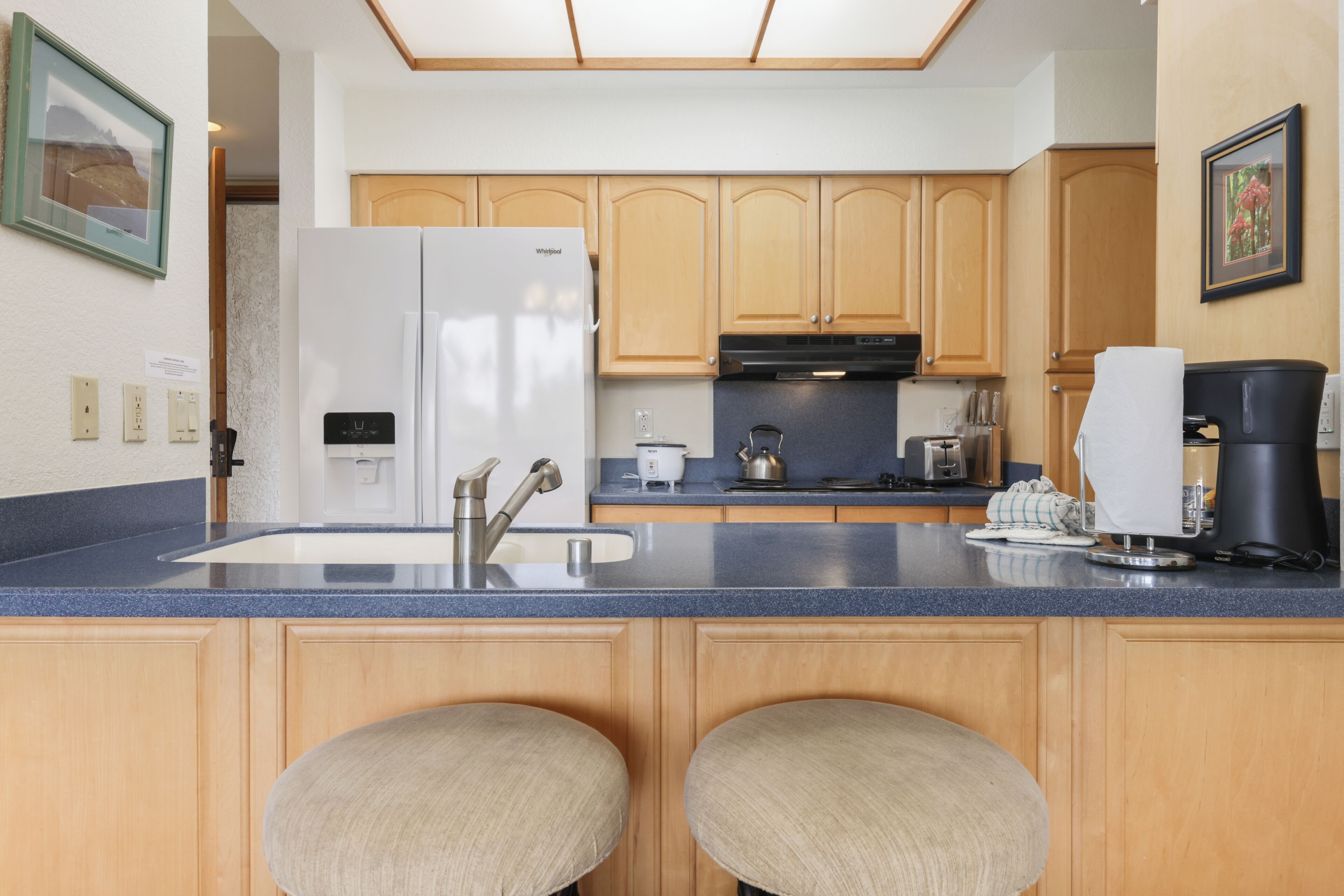 A kitchen with wooden cabinets, a white refrigerator, a sink, and two bar stools.