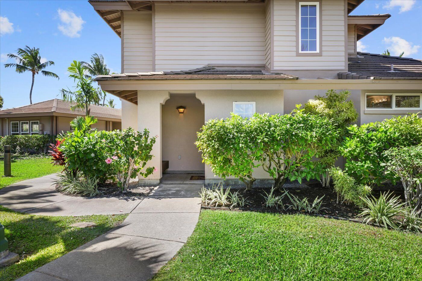 A two-story house with a covered entryway, a front yard with various plants, and a clear sky.