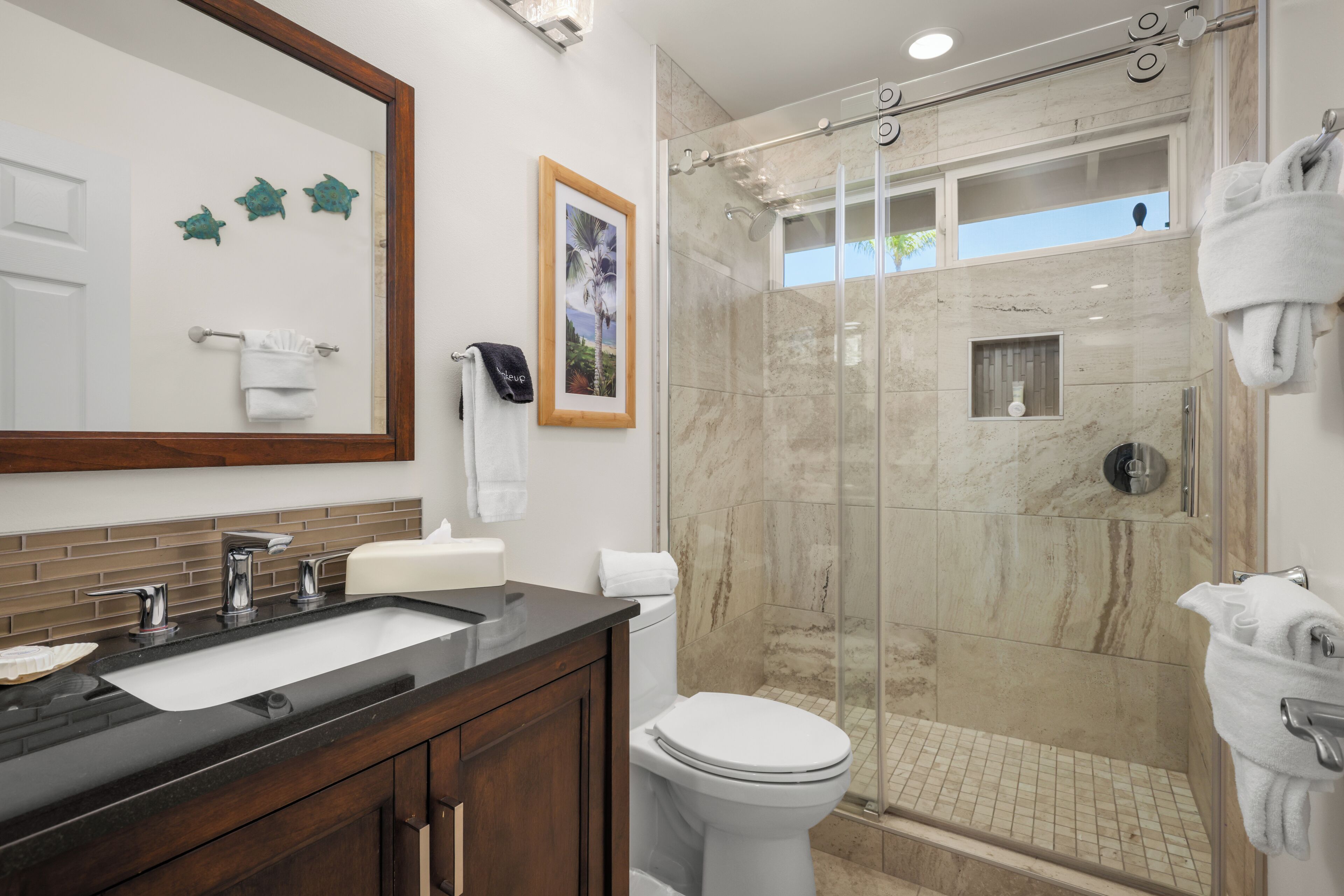 A bathroom with a marble shower, a sink with a vanity, and a toilet.