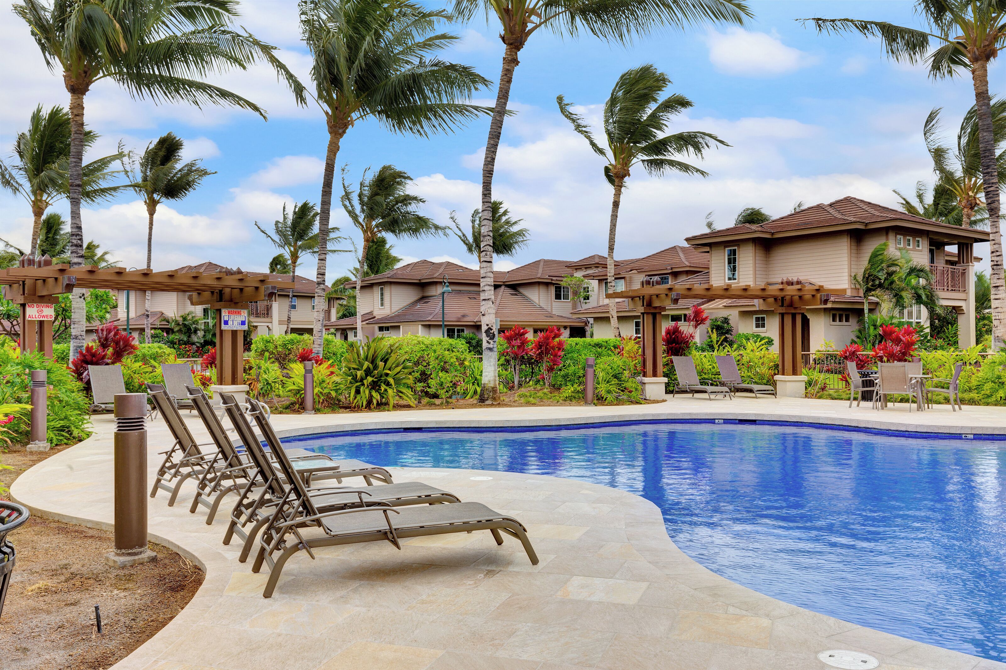 A resort with a swimming pool, lounge chairs, palm trees, and a clear sky.