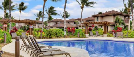 A resort with a swimming pool, lounge chairs, palm trees, and a clear sky.