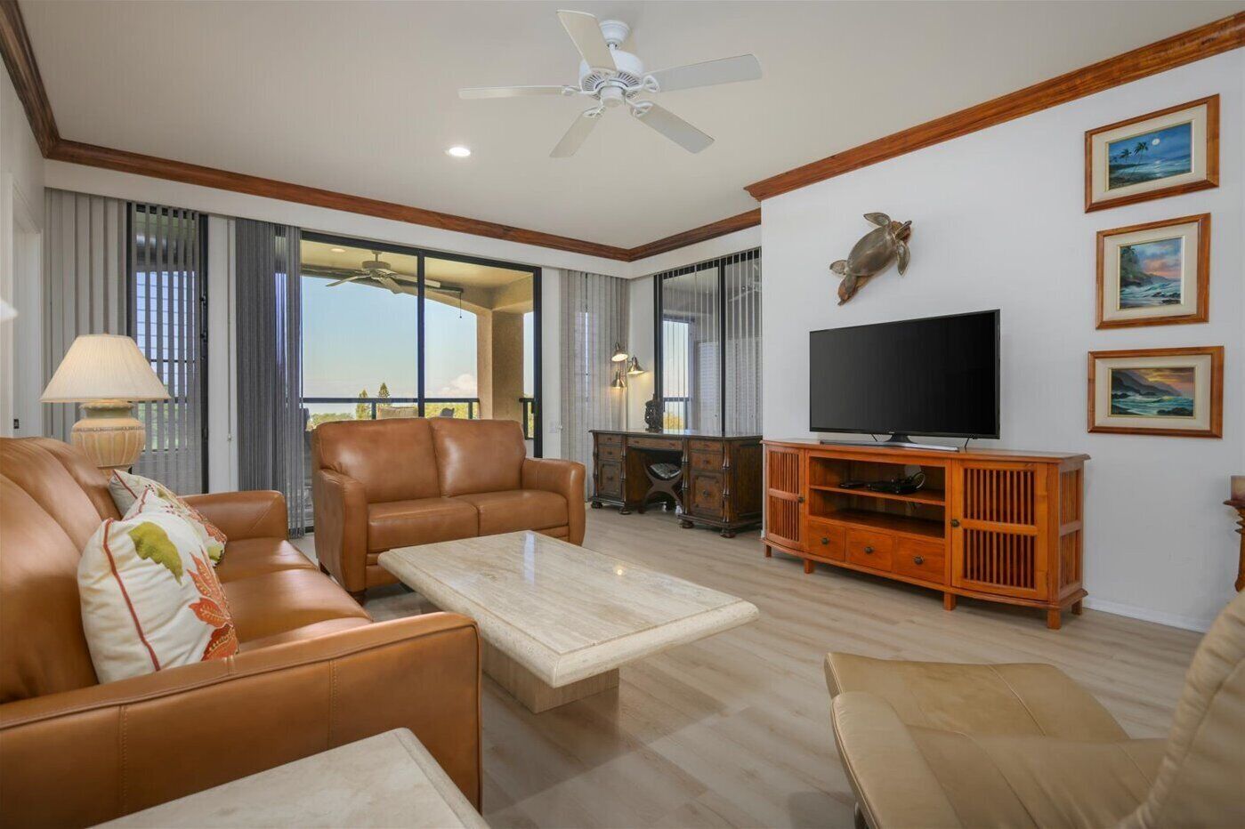 A living room with leather sofas, a coffee table, a TV on a wooden stand, and artwork on the walls.