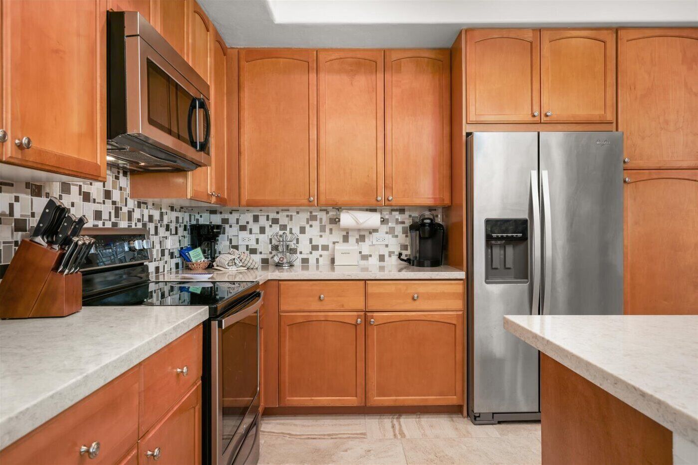 A kitchen with wooden cabinets, a stainless steel refrigerator, a microwave, and a coffee maker.