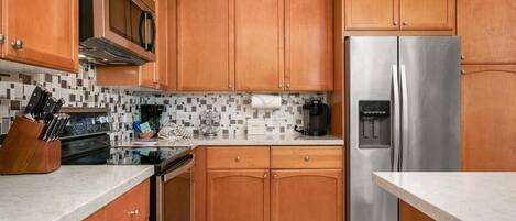 A kitchen with wooden cabinets, a stainless steel refrigerator, a microwave, and a coffee maker.