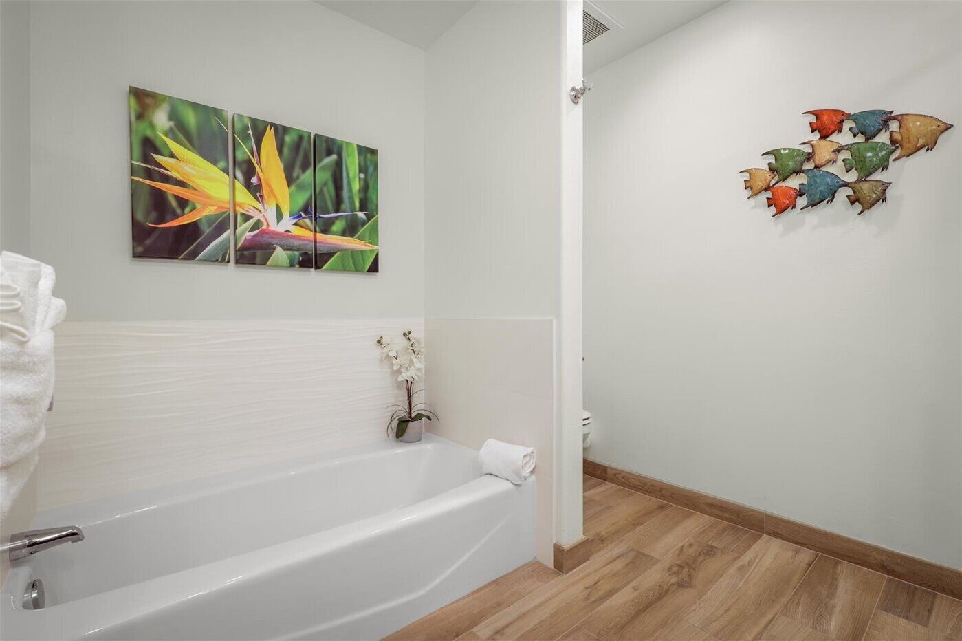 A bathroom with a bathtub, a wall-mounted orchid plant, and a colorful fish wall art piece.