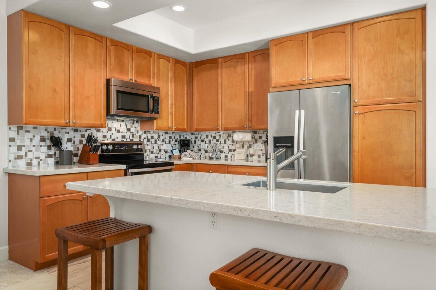 A modern kitchen with wooden cabinets, a stainless steel refrigerator, a microwave, and a tiled backsplash.