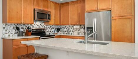 A modern kitchen with wooden cabinets, a stainless steel refrigerator, a microwave, and a tiled backsplash.