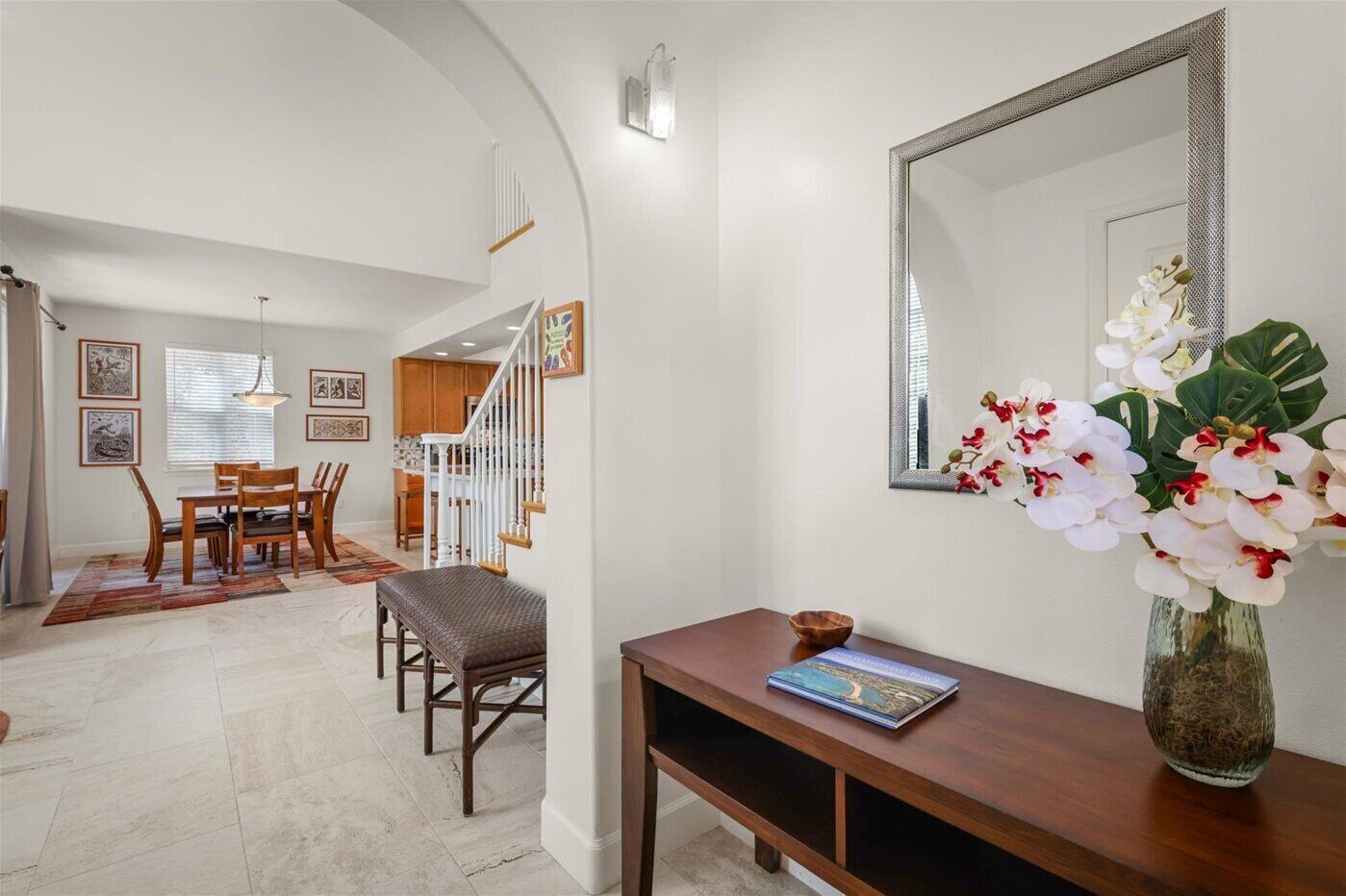 A modern living room with a dining area, a staircase, and a large mirror.