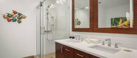 A modern bathroom with a glass shower enclosure, a large mirror, and a vanity with two sinks.