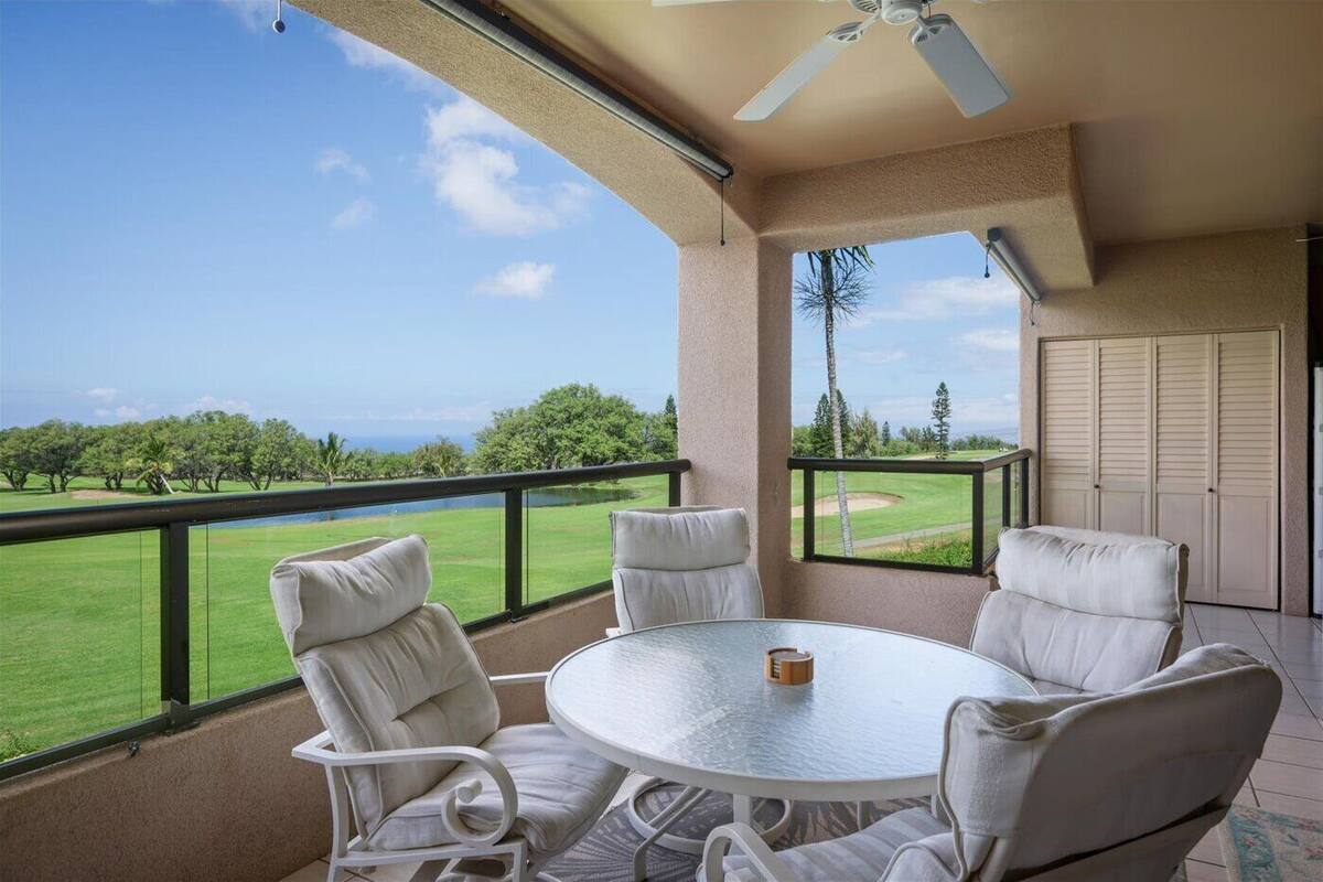 A balcony with a round table and four chairs, overlooking a golf course and a body of water.