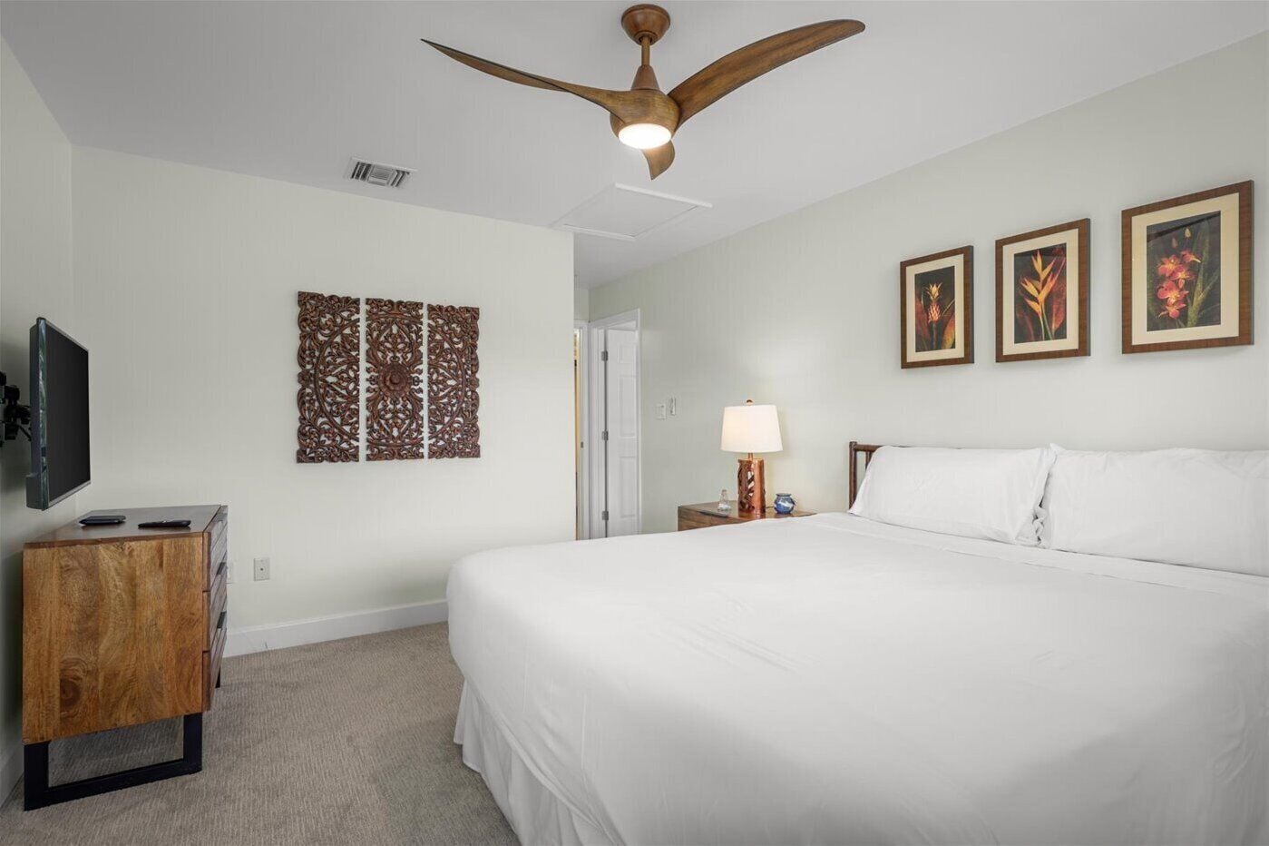 A hotel room with a large bed, a ceiling fan, a TV on a wooden cabinet, and three framed pictures on the wall.