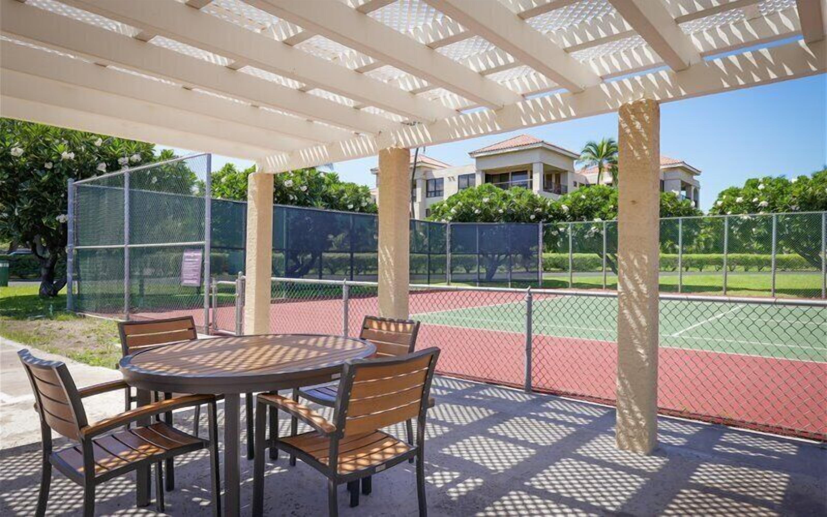 A covered outdoor seating area with a tennis court in the background.
