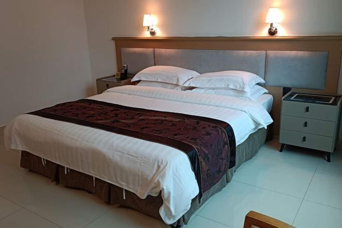 A hotel room with a large bed, two bedside tables, a nightstand, and a lamp.