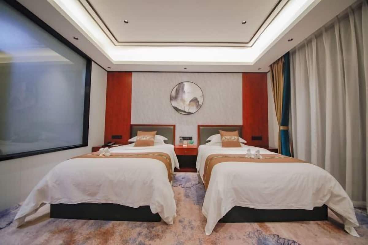 A hotel room with two beds, a large mirror, a TV, and a window.