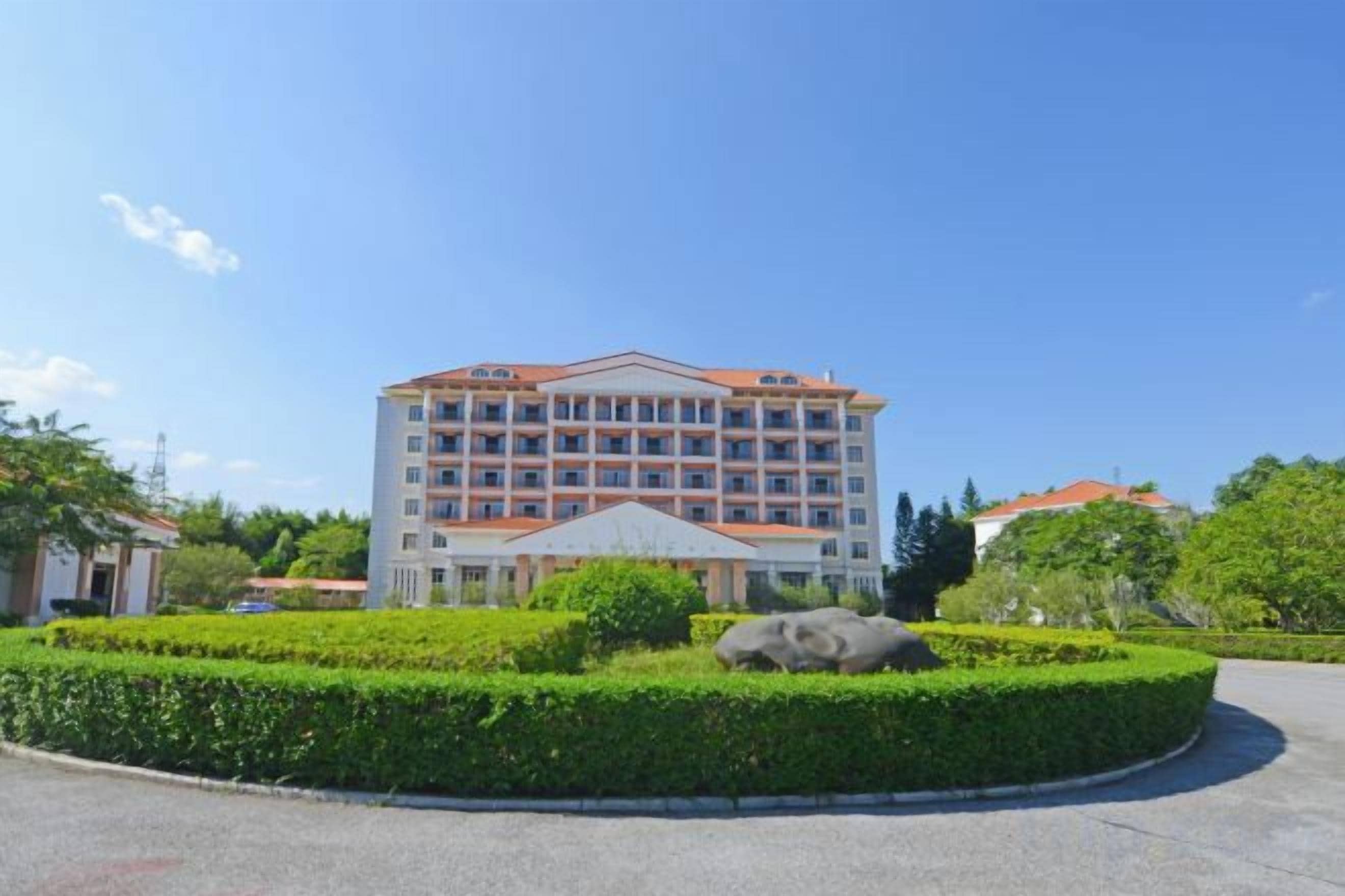 A multi-story hotel with a central courtyard, surrounded by greenery and a clear sky.