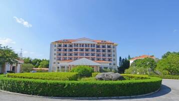 A multi-story hotel with a central courtyard, surrounded by greenery and a clear sky.