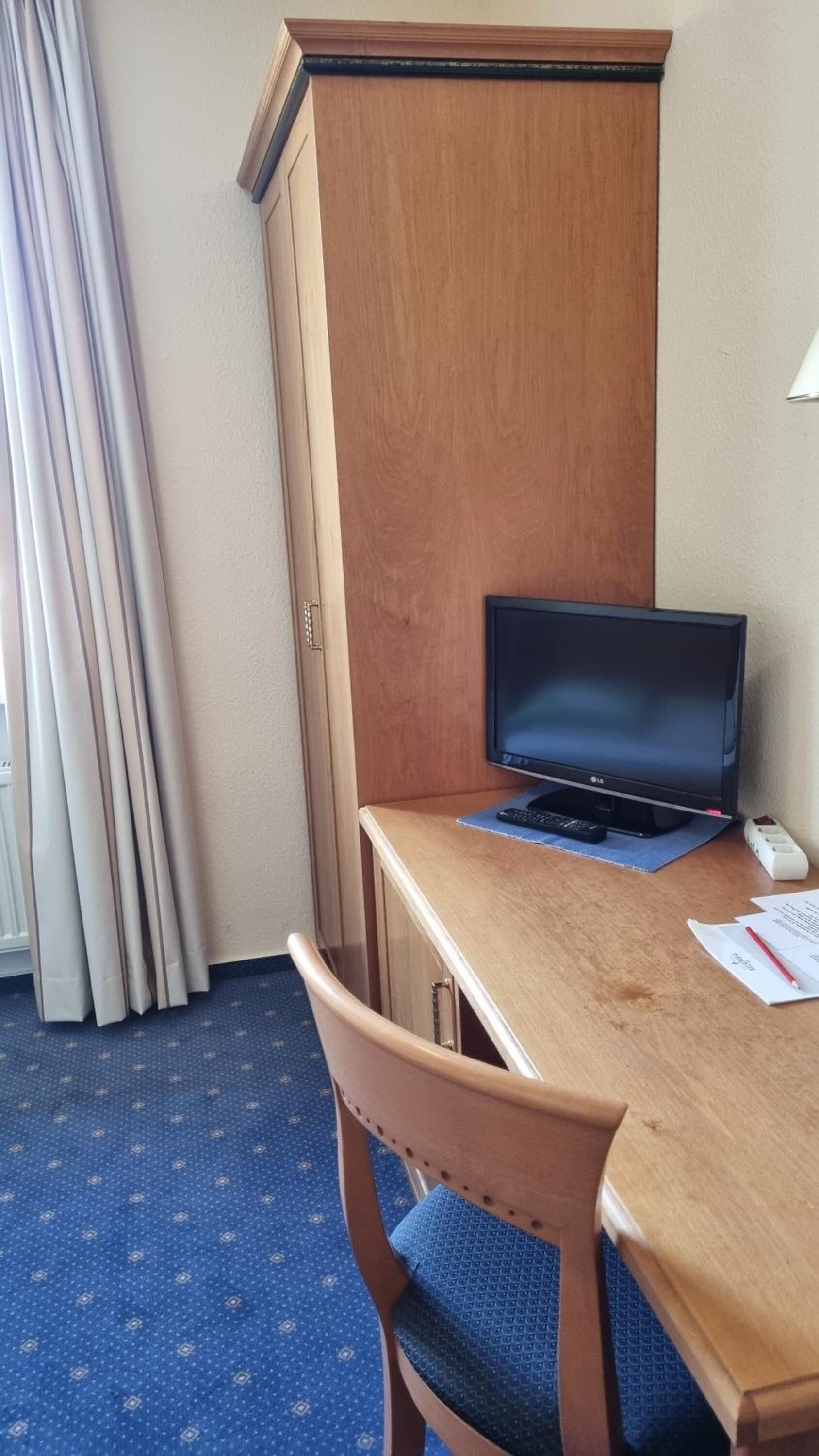Une chambre d’hôtel avec un bureau en bois, un ordinateur portable, une télécommande et une chaise.