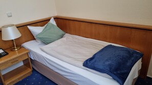 Una habitación de hotel con una cama individual, una mesita de noche con lámpara y un teléfono.