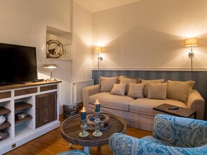 Un salón con sofá, una mesa de centro con velas, un televisor sobre un mueble bajo y lámparas fijadas a la pared.