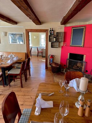 Un comedor con una mesa de madera dispuesta para una comida, una chimenea y una pared roja con un cuadro enmarcado.