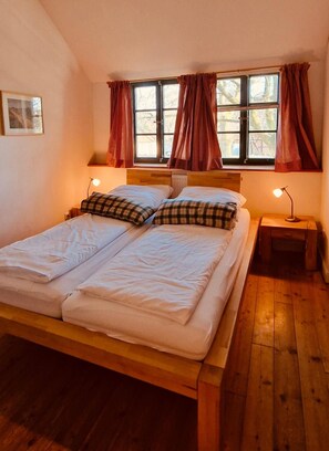 Una cama doble con estructura de madera, dos mesitas de noche con lámparas y una ventana con cortinas.